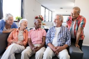 A group of 5 senior men and women sitting together on a couch laughing and having a conversation in their independent living community