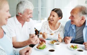 Two senior couples eating breakfast with a cup of coffee in the dining room of their senior living community