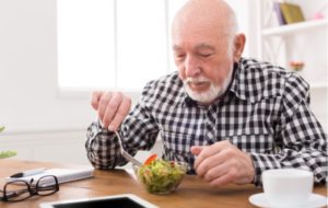 A senior citizen man sitting at a dining table eating a small salad