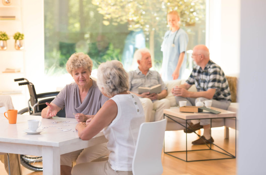 A group of seniors sitting socializing indoors engaged in various activities such as reading and conversing with each other.