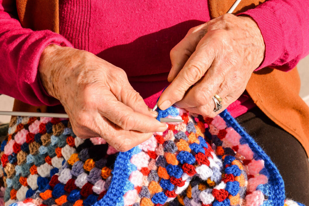 A close up of a senior knitting a blanket on her lap as an enriching activity in a senior living community