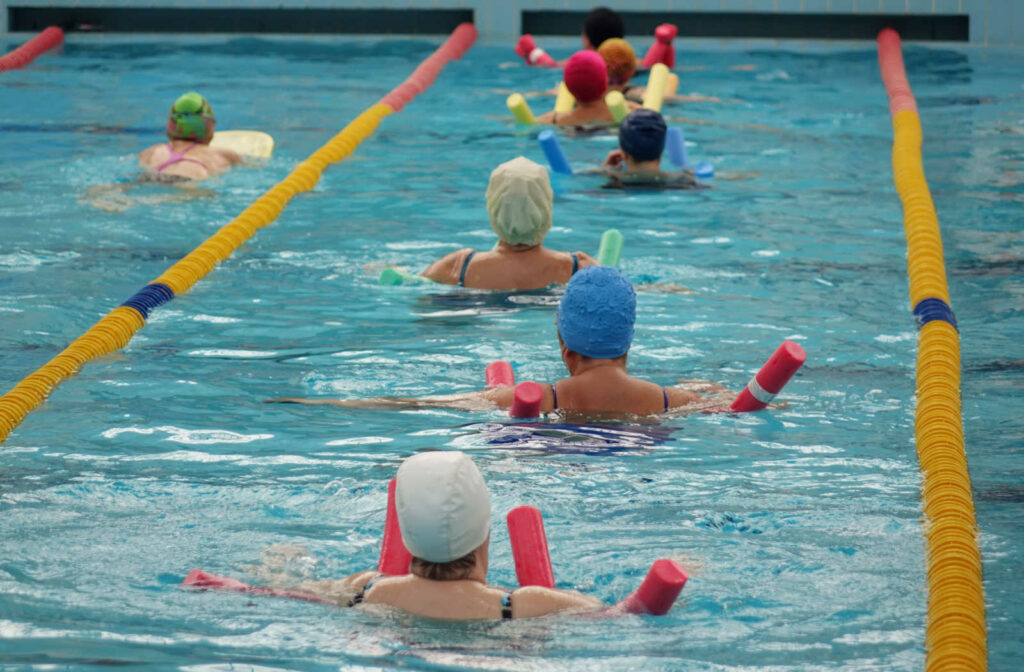 A group of solder adults is using pool foam noodles while doing water aerobics.