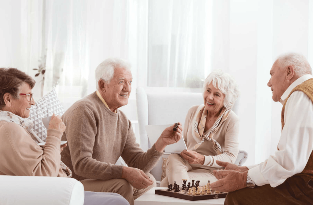 A group of 4 senior living residents playing chess and engaging in conversation.