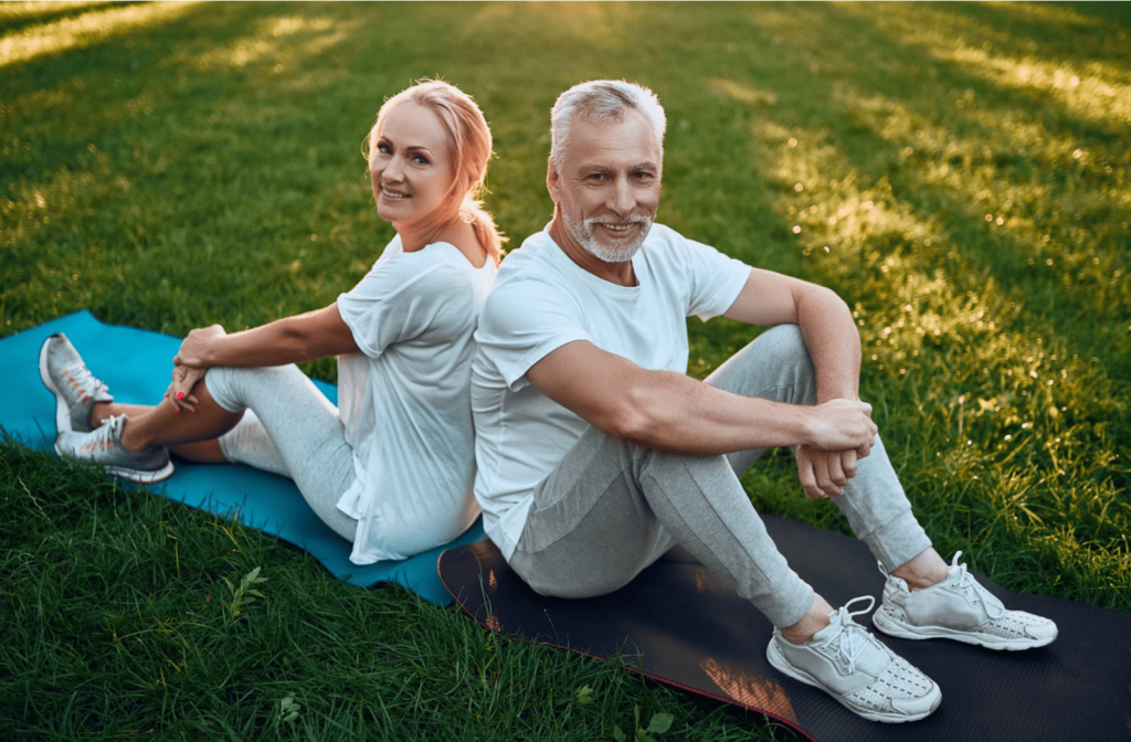 A middle-aged couple stretching on yoga mats on a lawn