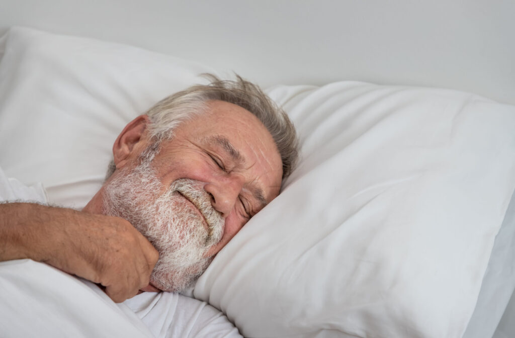 A senior man with white hair sleeping alone on a bed with his eyes closed.