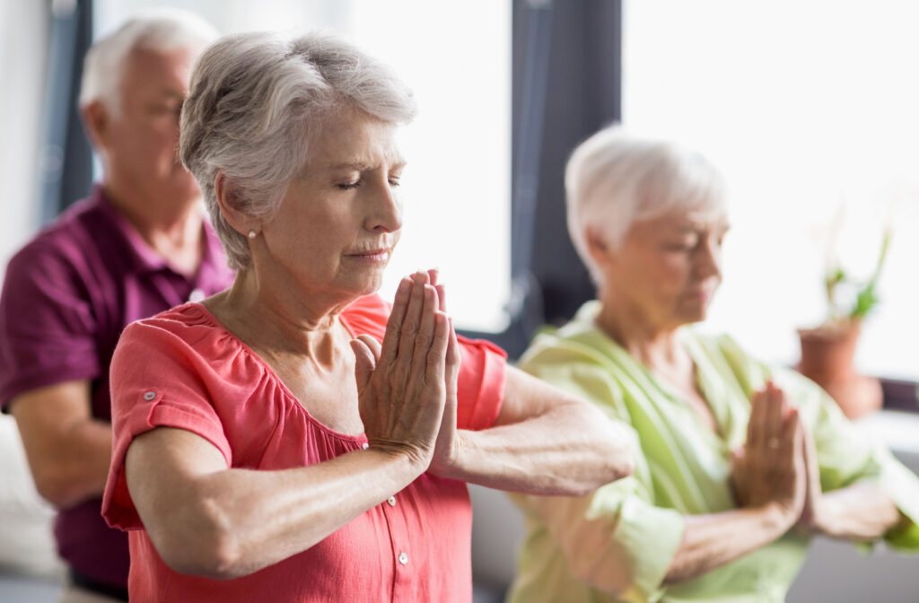 A group of seniors with closed eyes practicing yoga and are sitting on yoga mats.