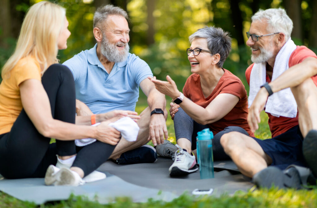 4 seniors  sitting on yoga mats in a park and chatting.