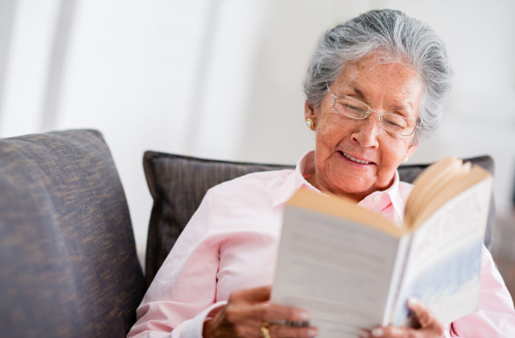 A senior woman smiling, sitting on a couch and reading a book.