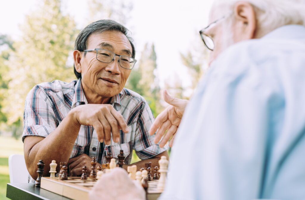 Two older adult men sitting across from each other playing a game of chess in a park