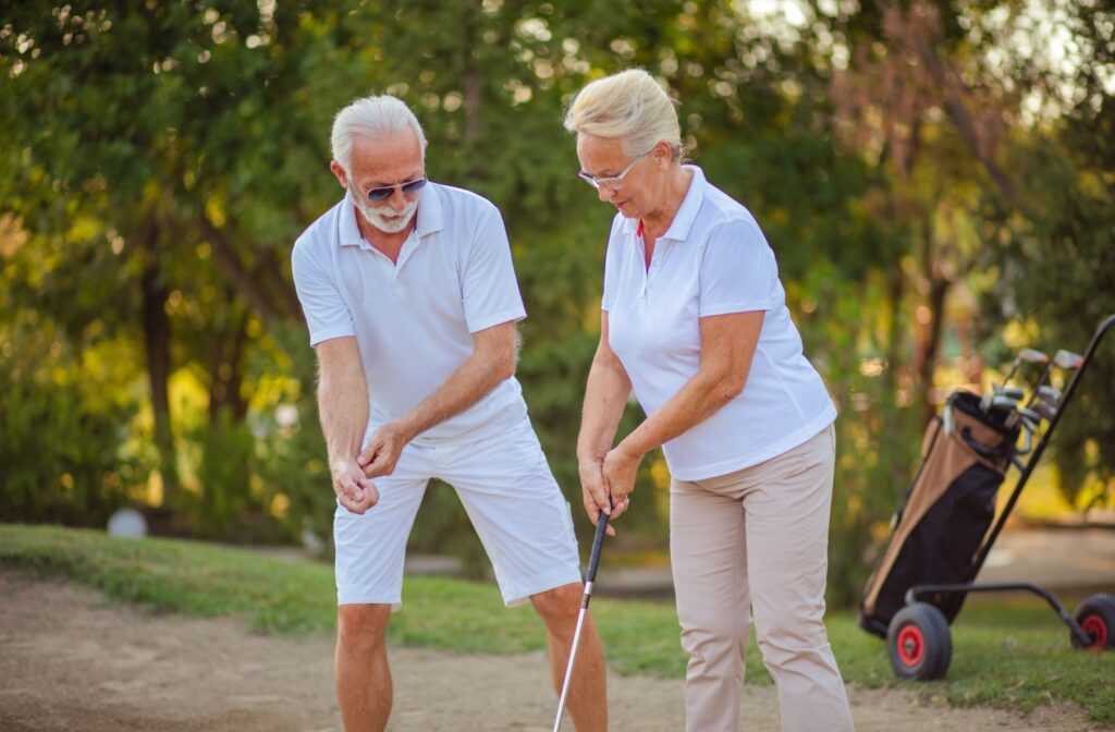 An older adult man teaching an older adult woman how to play golf