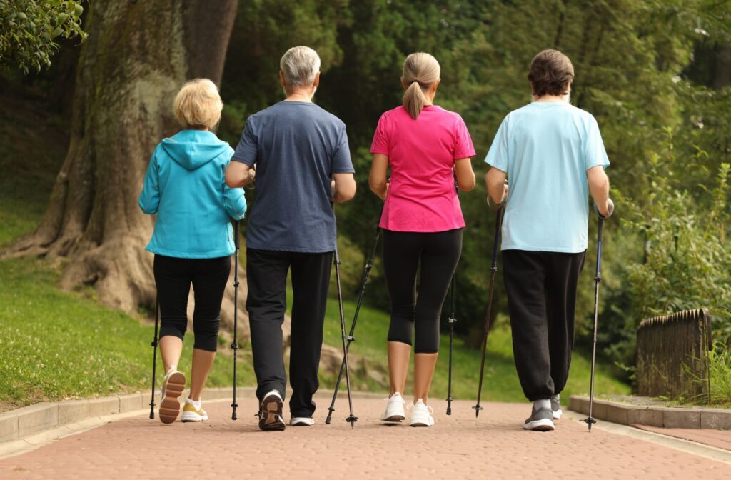 A behind view of a group of older adults walking on a path with walking sticks.