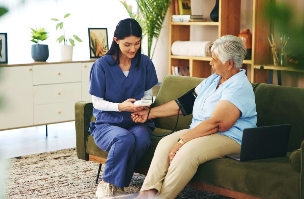Healthcare professional checking blood pressure of an older adult seated on a couch in a senior living community