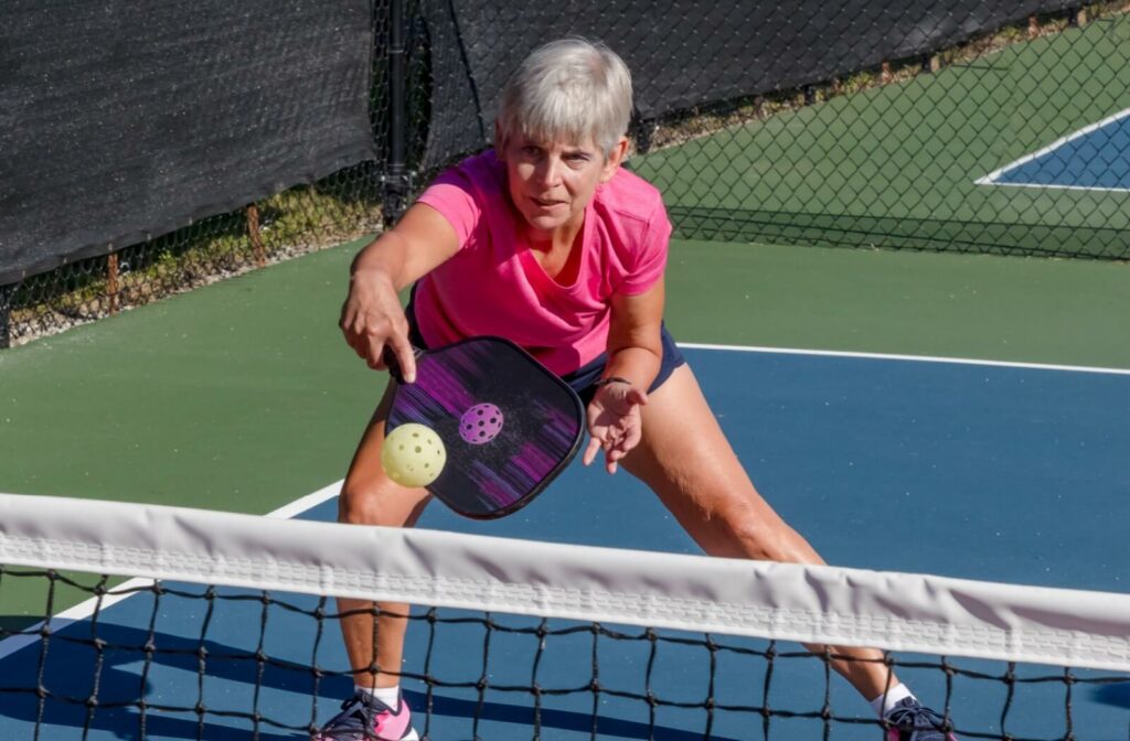 Older adult playing pickleball on an outdoor court mid game focused on hitting the ball with a paddle near the net