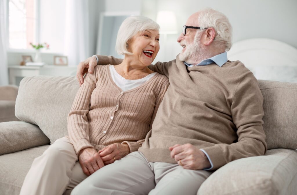 A joyful older couple sits on a couch, smiling at each other as they enjoy independent living.