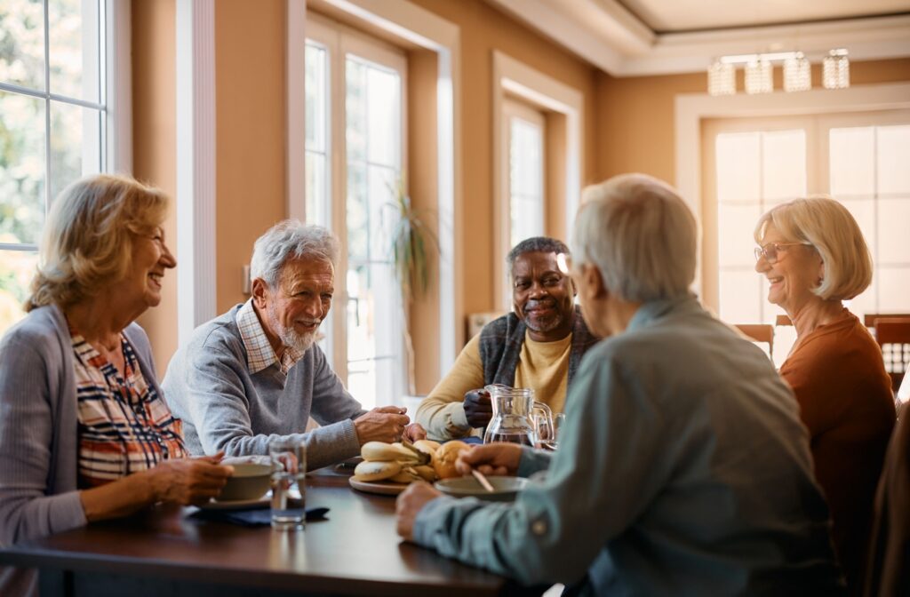 A group of seniors enjoy conversation together during lunch at a dining table in a senior living community.