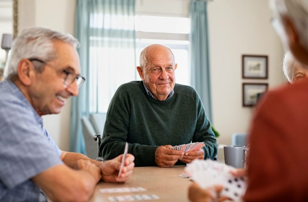 An older adult is smiling and playing cards with friends in an independent living community.