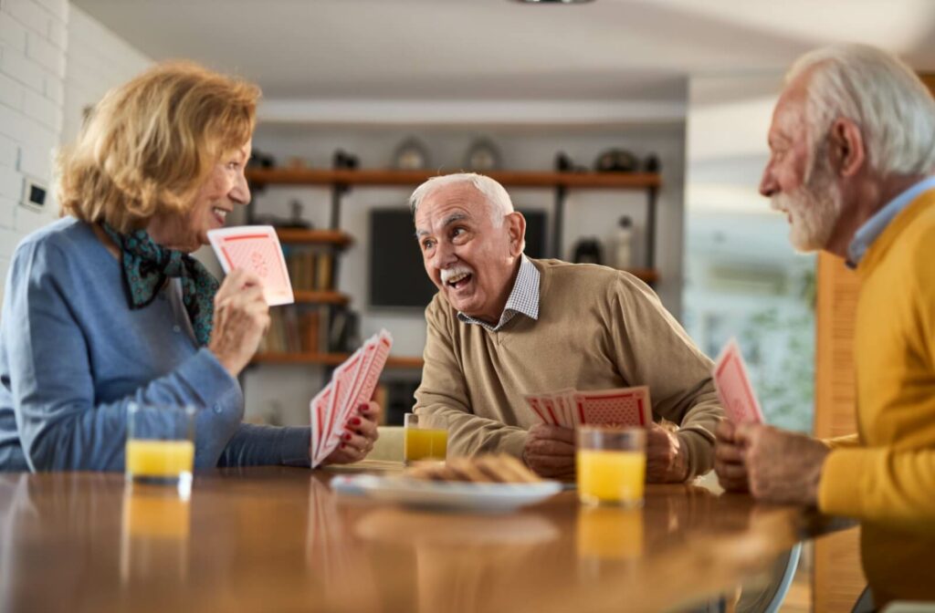A group of seniors smile and laugh while playing with jumbo cards and drinking orange juice.