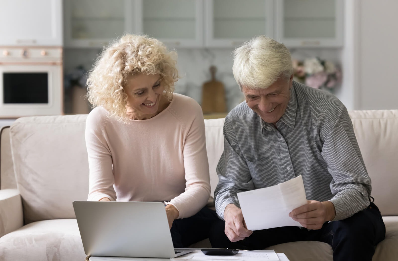 A retired couple sit on a couch while reviewing their finances.
